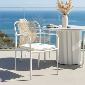 Evone Aluminium Rope Outdoor Dining Chairs Set of 4 in Natural, featuring a white metal frame, woven rope backrest, and white seat cushion, elegantly arranged on a terrace overlooking the ocean.