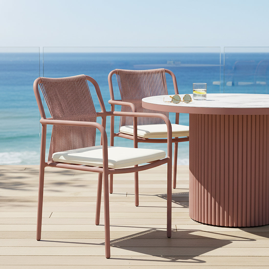 Evone Aluminium Rope Outdoor Dining Chairs Set of 4 in Terracotta, featuring metal frames with rope backs and cushioned seats, paired with a round table on a seaside deck with ocean view.