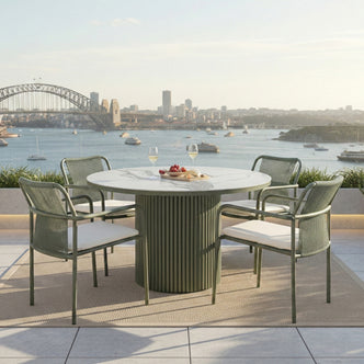 Evone 4 Seater Stone Outdoor Dining Table Set in Green with marble top, rope-back chairs, cheese board, and wine, set on a terrace with a harbor and bridge view.