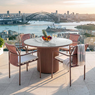 Evone 4 Seater Stone Outdoor Dining Table Set in Terracotta features a marble top and four rope-style armchairs. A bowl of fruit and champagne flutes enhance the sunlit rooftop ambiance.