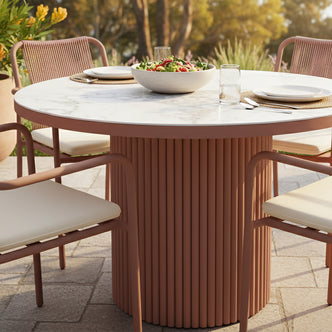 Evone Aluminium Outdoor Dining Table in Terracotta with a marble-like top, surrounded by matching chairs with light cushions and rope backs, set for a meal on a paved patio.