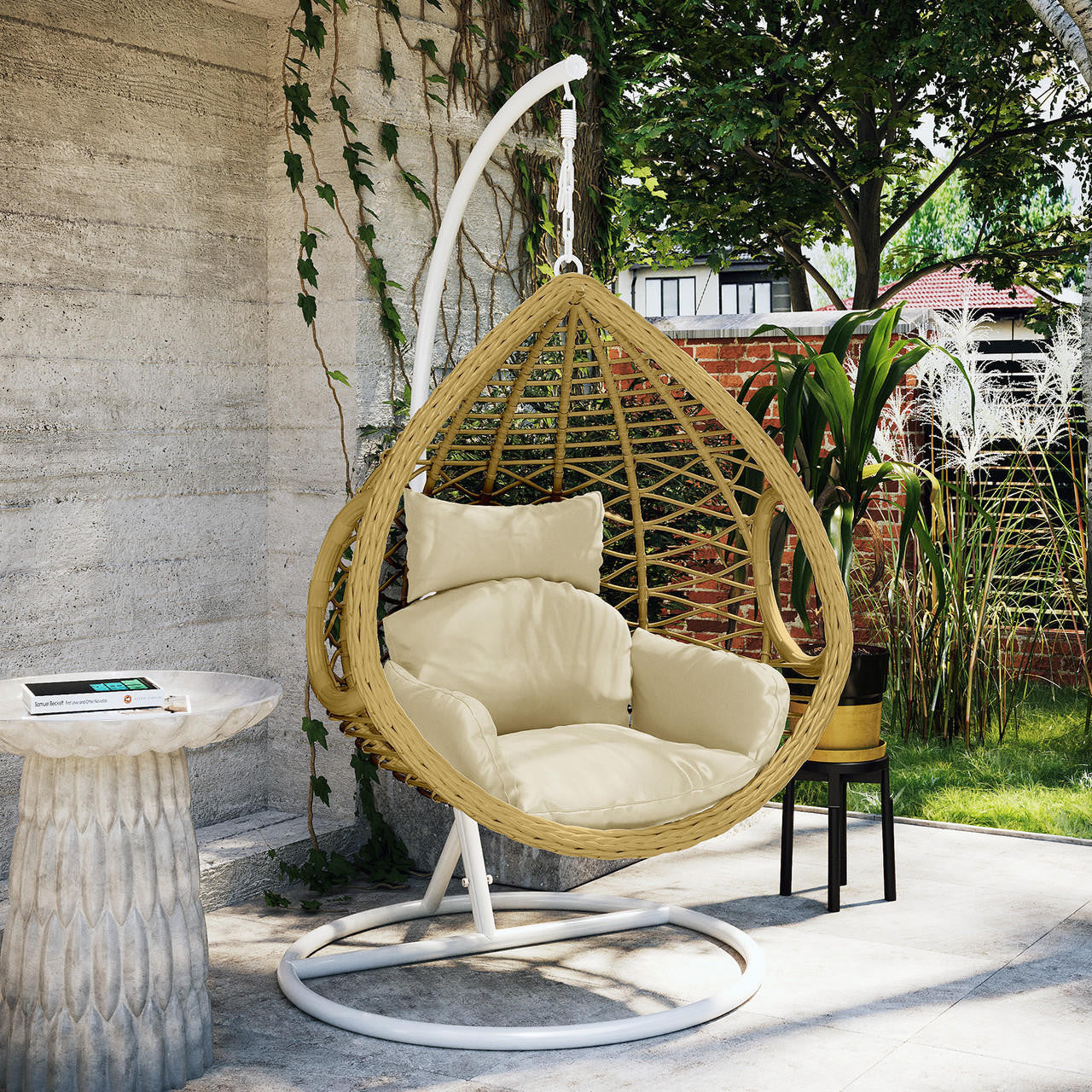 Hilda Large Outdoor Hanging Egg Chair & Cushion in Natural, featuring a woven rattan-style design with plush cream cushions, suspended from a white metal stand, set in a lush garden nook.