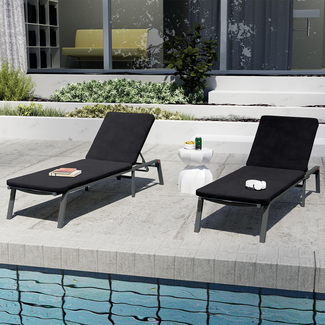 Jabari Outdoor Sun Loungers with Cushions Set of 2 in Black on a poolside deck, featuring adjustable backs, a white side table with snacks, books, and headphones nearby.