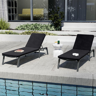 Jabari Outdoor Sun Loungers with Cushions Set of 2 in Black on a poolside deck, featuring adjustable backs, a white side table with snacks, books, and headphones nearby.