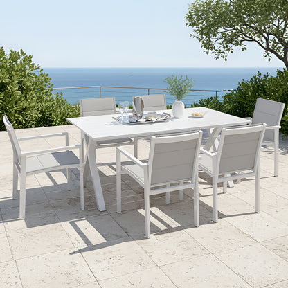Jensen 6 Seater Aluminium Outdoor Dining Set in Light Grey features a sleek white table with matching armchairs, adorned with a ceramic vase, metal tray, and snacks, overlooking a serene ocean view.