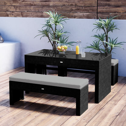 Kummi 4 Seater Outdoor Dining Bench Set features a black wicker table with glass top, apples, juice bottles, and glasses, paired with cushioned benches, and accented by potted tropical plants.