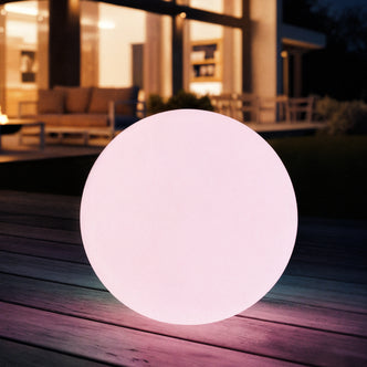 Sphero 40cm Floating Waterproof Outdoor LED Ball Lights on a wooden deck, emitting a soft pink glow in front of a modern house, showcasing its captivating outdoor illumination.
