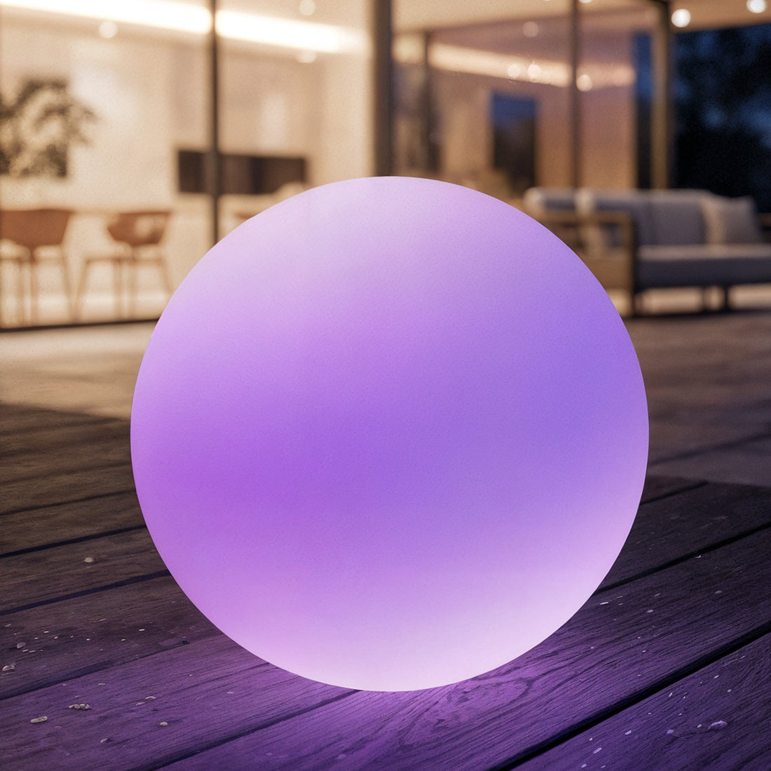Sphero 50cm Floating Waterproof Outdoor LED Ball Lights glowing soft purple on a wooden deck, enhancing a patio with ambient illumination; visible through glass doors, a modern home's interior.