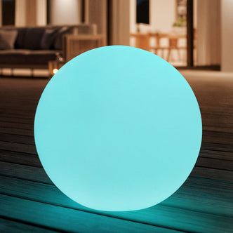 Sphero 60cm Floating Waterproof Outdoor LED Ball Lights softly glowing on wooden decking, set against a modern indoor/outdoor living space with a visible sofa and dining area through a sliding door.