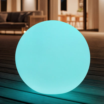 Sphero 60cm Floating Waterproof Outdoor LED Ball Lights softly glowing on wooden decking, set against a modern indoor/outdoor living space with a visible sofa and dining area through a sliding door.