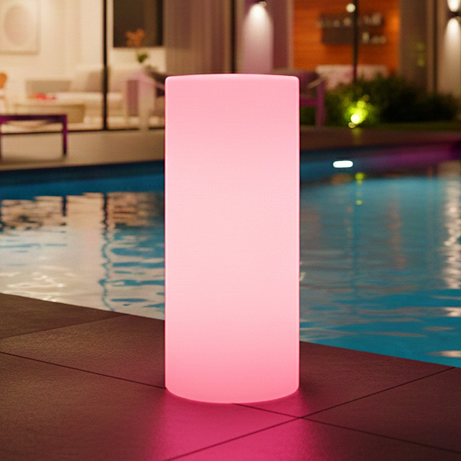 The image features the 16 Colour Outdoor LED Bollard Light in Multicolour, glowing warmly beside a pool on a tiled deck, with its pink hue reflecting in the water, enhancing the serene ambiance.