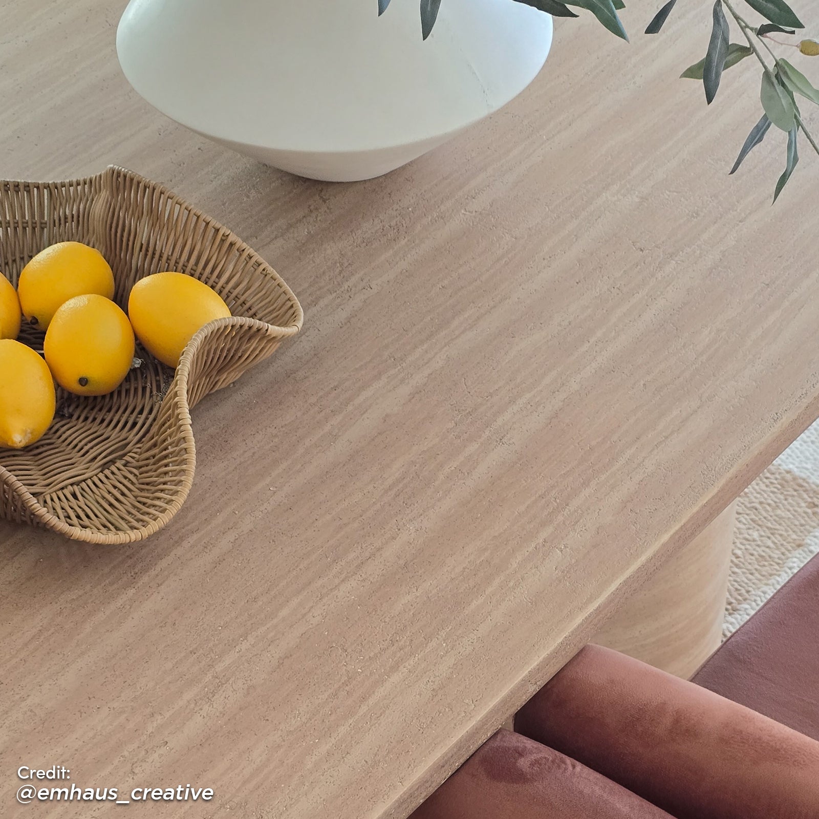 Lumen 220cm Oval Outdoor Concrete Dining Table in Beige with a sleek, oval top and cone-shaped base, surrounded by wicker bowl of lemons and white vase with green branches on a light wood tabletop.