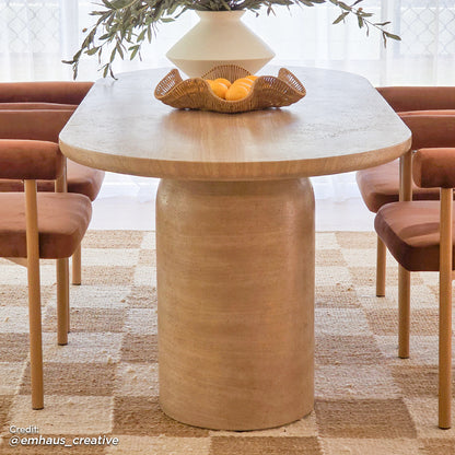 Lumen 220cm Oval Outdoor Concrete Dining Table in Beige, featuring an elegant oval shape and cone-shaped base, set on a textured jute rug with rust-colored chairs and a rattan bowl of oranges.