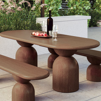 Lumen 220cm Oval Indoor/Outdoor Concrete Dining Table Chestnut features an elegant oval shape with a cone-shaped base, set on a coffee table alongside pomegranates and a wine glass.