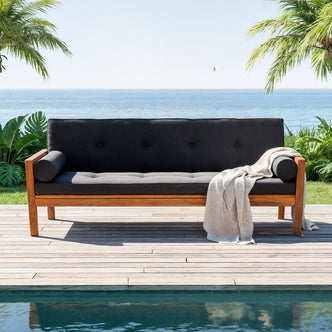 Luxo Meves Hardwood Outdoor Daybed Sofa & Cushion in Black, featuring a wooden frame with dark gray cushions and bolster pillows, set on a deck beside a pool with tropical ocean view.