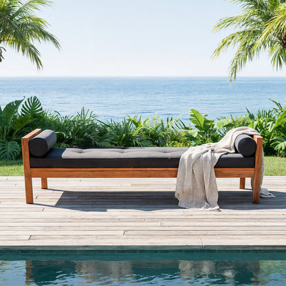 Luxo Meves Hardwood Outdoor Daybed Sofa & Cushion in Black, featuring a teak-like frame, dark gray cushions with bolsters, and a draped throw, set on a poolside deck amidst tropical greenery.