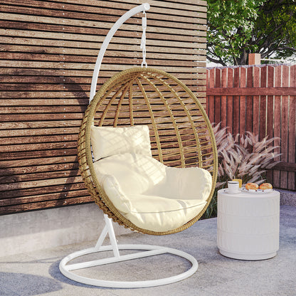 Napili Outdoor Rattan Egg Chair with Cushion in Cream White, featuring a suspended woven rattan design, thick cushion, and matching back pillow, situated beside a small white side table with refreshments.
