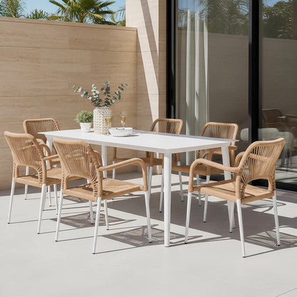 Navarre 6 Seater Aluminium Outdoor Dining Set in Natural features a white table with six wicker-style chairs, complemented by a ceramic vase, potted plant, glasses, and a serving bowl on a patio.