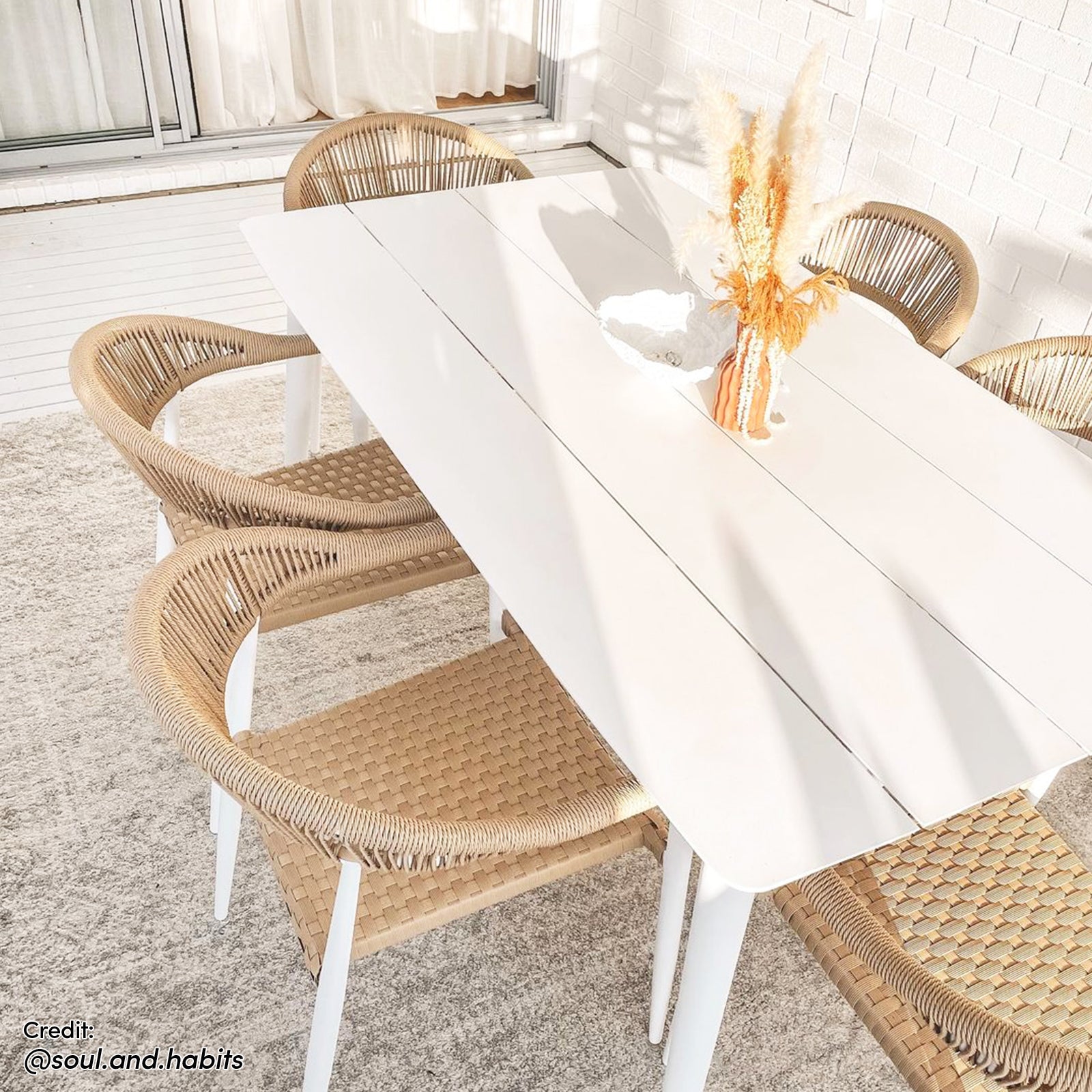 Nemma 6-Seater Aluminium Outdoor Dining Set Natural, featuring a sleek table with a wicker finish and six matching chairs, set on a white carpet in a bright, airy room.