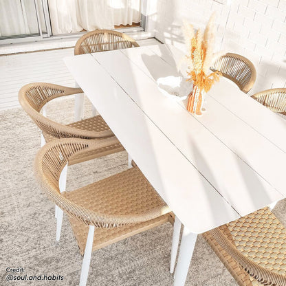 Nemma 6-Seater Aluminium Outdoor Dining Set Natural, featuring a sleek table with a wicker finish and six matching chairs, set on a white carpet in a bright, airy room.