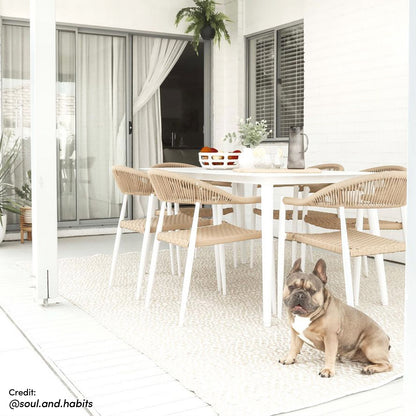 Nemma 6-Seater Aluminium Outdoor Dining Set Natural, featuring a sleek table with six chairs, set on a patio with a rug, plant, and window, showcasing its suitability for outdoor gatherings.
