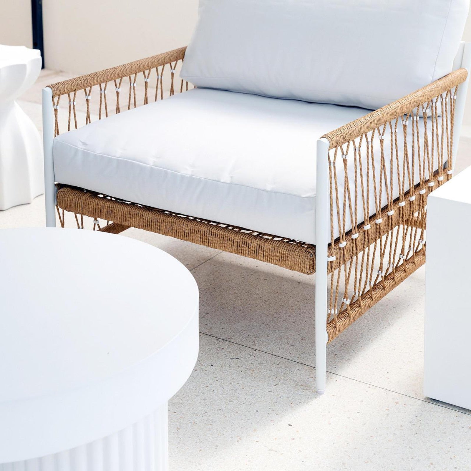 Nuevo 4 Seater Wicker Outdoor Lounge Set in Light Beige, featuring a modern white metal frame, thick white cushions, and natural-colored rope detailing, situated in a bright, minimalist space with a round table edge.