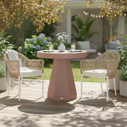 Orson 80cm Round Concrete Dining Table in Mocha Mousse on a patio, topped with daisies in a vase, place settings, and iced drinks, flanked by woven-rope armchairs with white cushions.