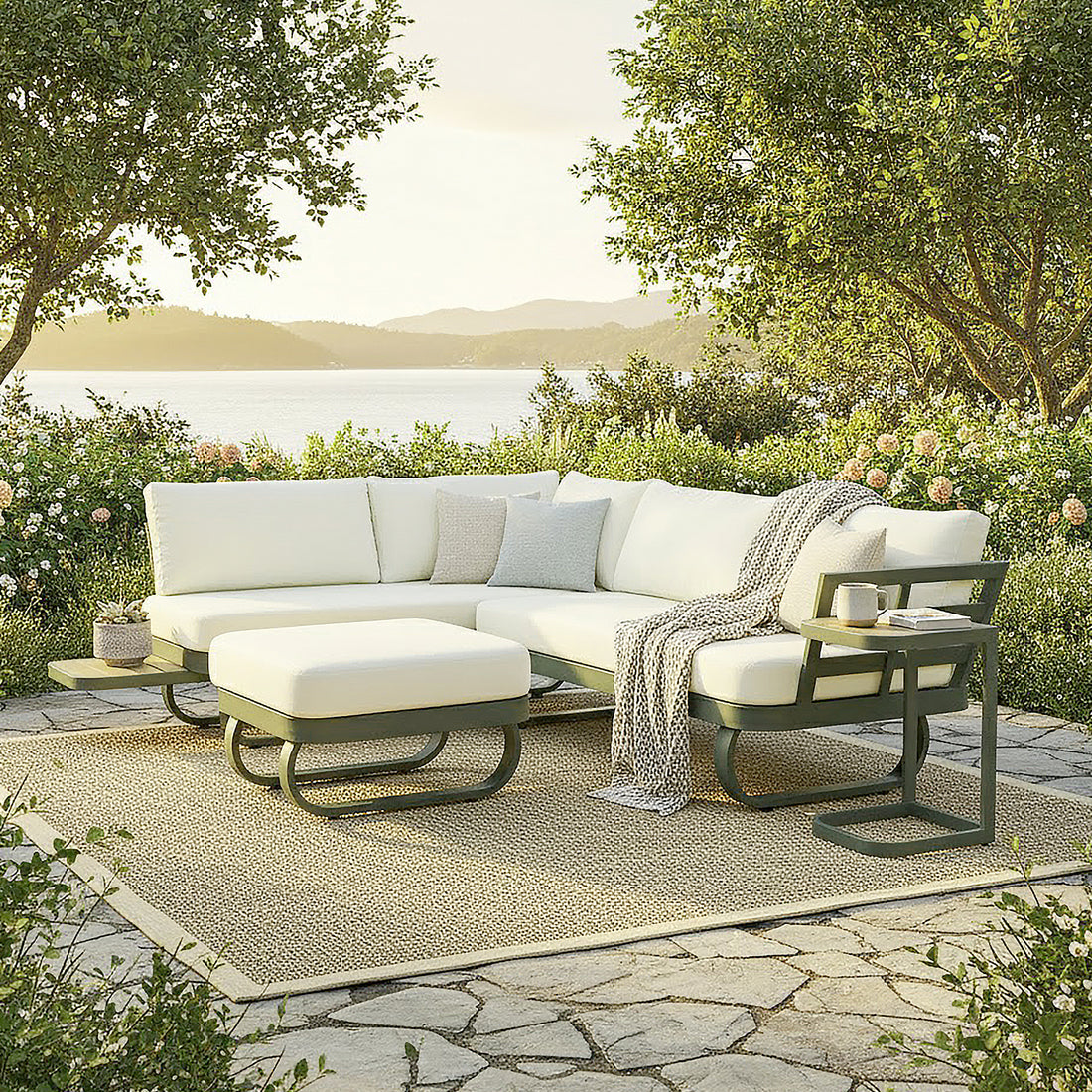 Paloma Modular Outdoor Lounge Set in Olive Green on a stone terrace, featuring an L-shaped sectional with pale cream cushions, a matching ottoman, and a small side table with a mug and book.