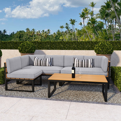 Panaluu 5 Seater Aluminium Corner Outdoor Lounge in Grey, featuring an L-shaped sofa with light-gray cushions, striped pillows, a matching coffee table, and a backdrop of lush greenery and palm trees.
