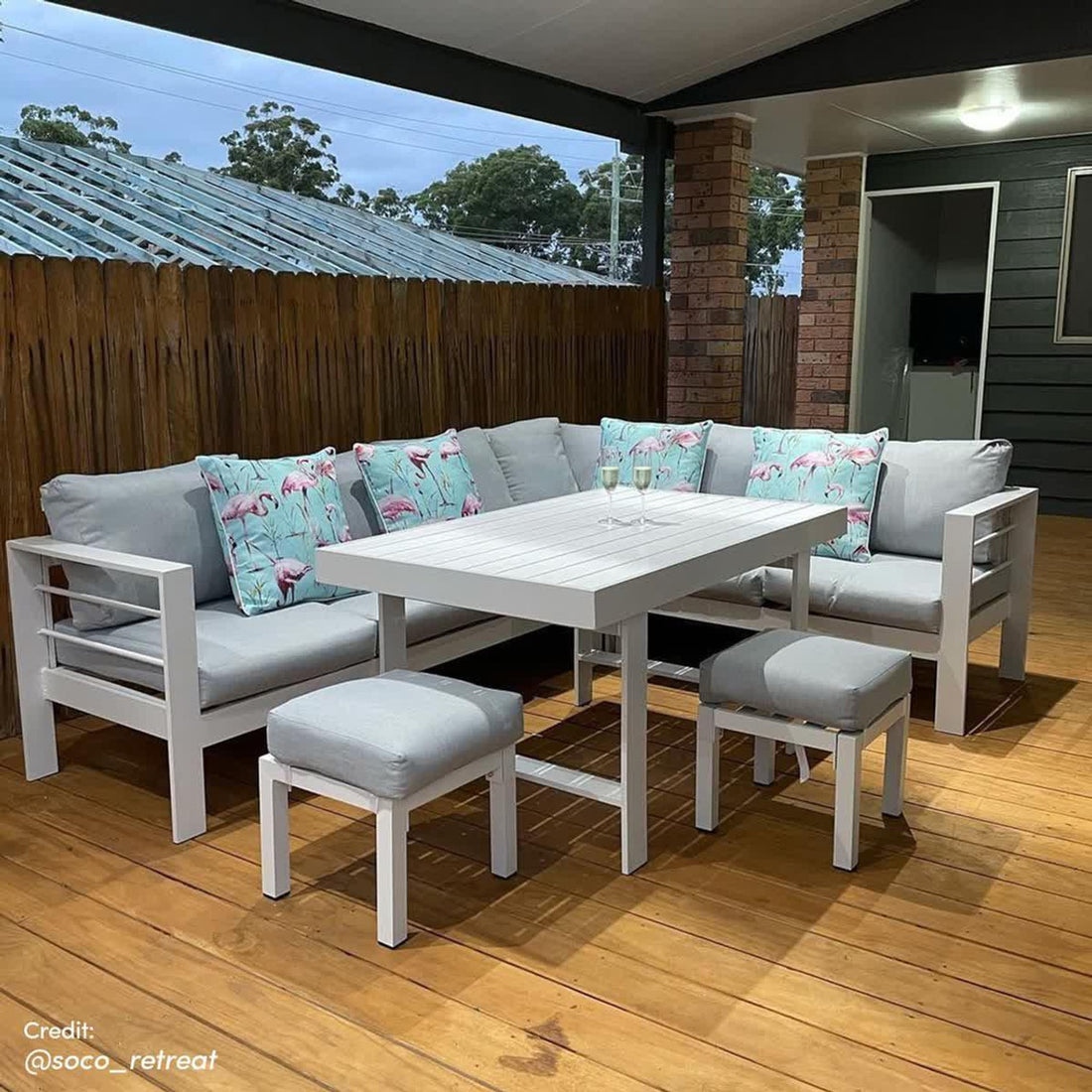 Portland Outdoor Corner Sofa Lounge with Footstools, featuring plush grey cushions on a robust frame, paired with a matching white stool and pillow adorned with flamingos, enhancing any outdoor setting.