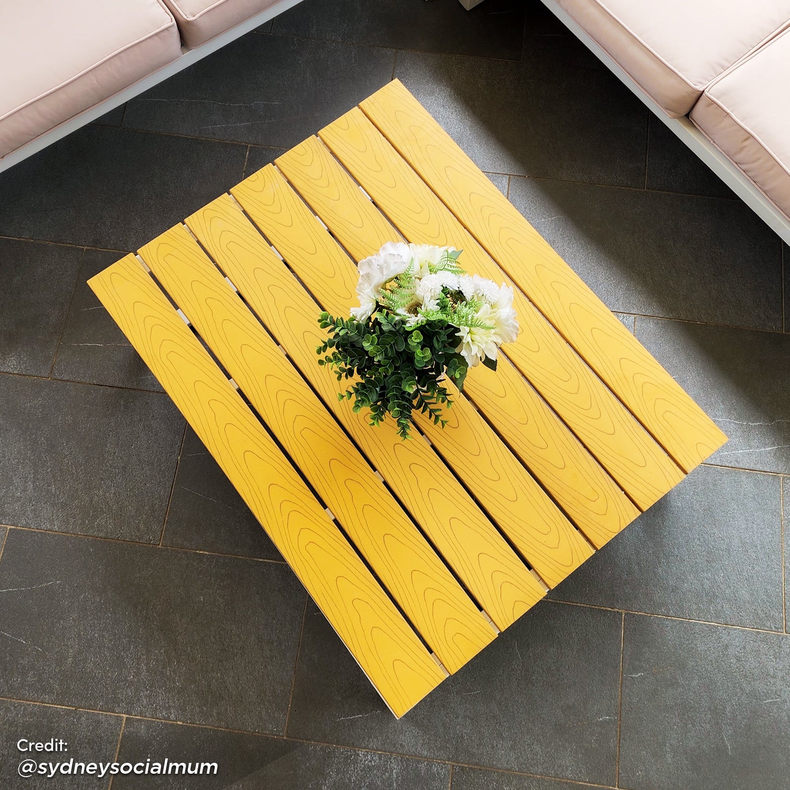 Rosa 5 Seater Outdoor Corner Sofa Lounge with Coffee Table displayed on a yellow wood surface, surrounded by green plants, highlighting its modern design and spacious seating arrangement.