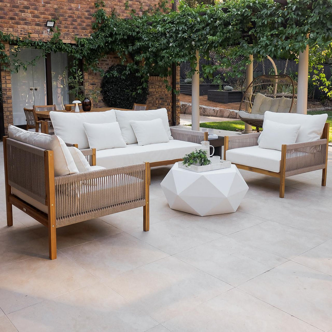 Savin 4-Seater Hardwood Outdoor Sofa Set in Beige features light wood frames, woven-rope sides, and plush off-white cushions, surrounding a white coffee table with a potted plant, enhancing outdoor elegance.