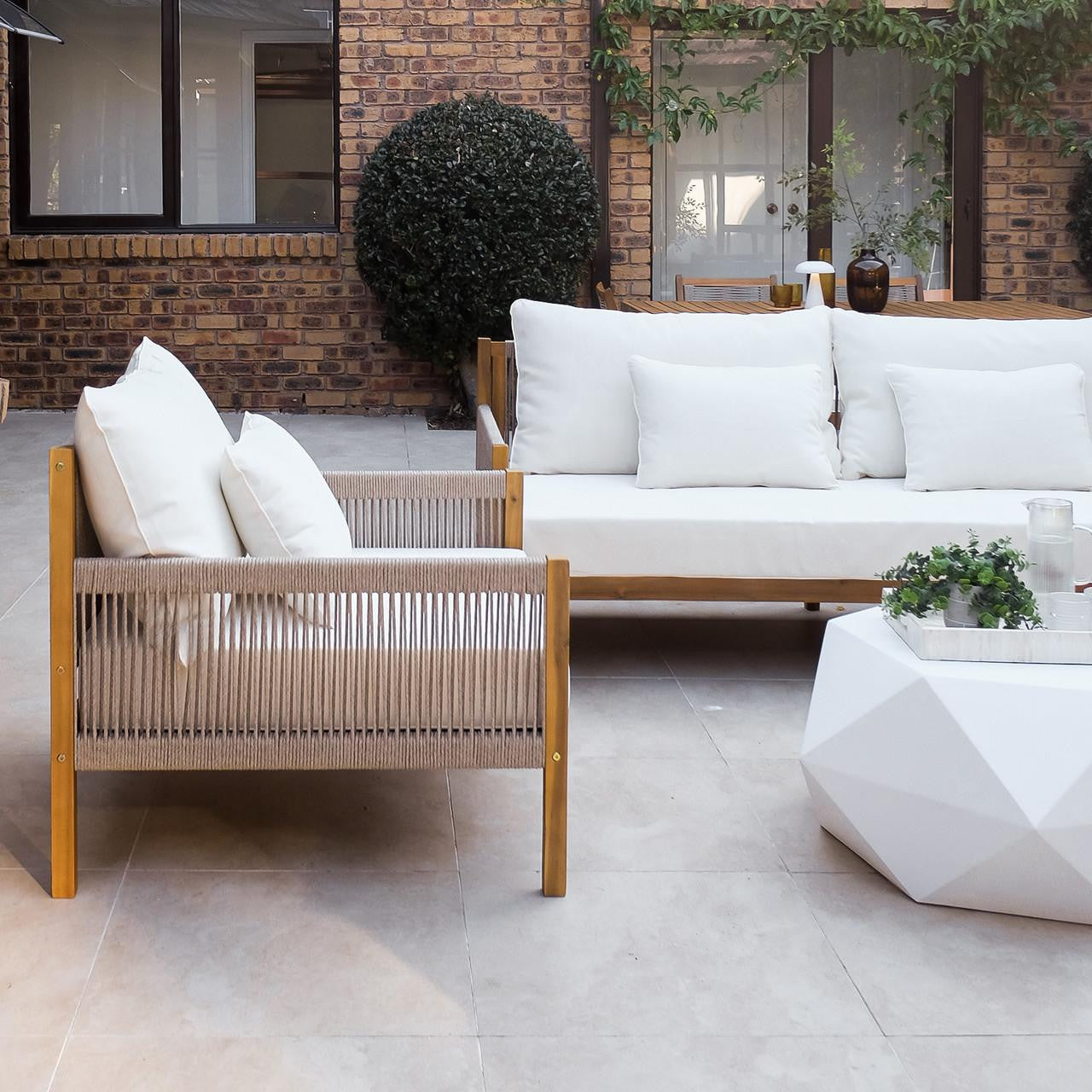 Savin 4-Seater Hardwood Outdoor Sofa Set in Beige on a tiled patio, featuring wooden frames, woven rope sides, and white cushions, complemented by a geometric coffee table with a plant and glass pitcher.