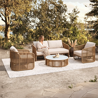 Solari 4 Seater Wicker Outdoor Sofa Set in Natural on a terrace, with plush cushions, includes a loveseat, two armchairs, and a round coffee table, creating a serene lakeside lounge atmosphere.