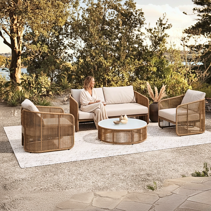 Solari 4 Seater Wicker Outdoor Sofa Set in Natural on a terrace, with plush cushions, includes a loveseat, two armchairs, and a round coffee table, creating a serene lakeside lounge atmosphere.