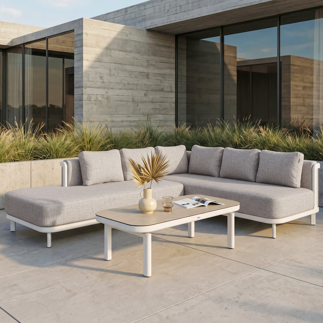 Outdoor sectional sofa and coffee table arranged on a patio with greenery and a modern home in the background.