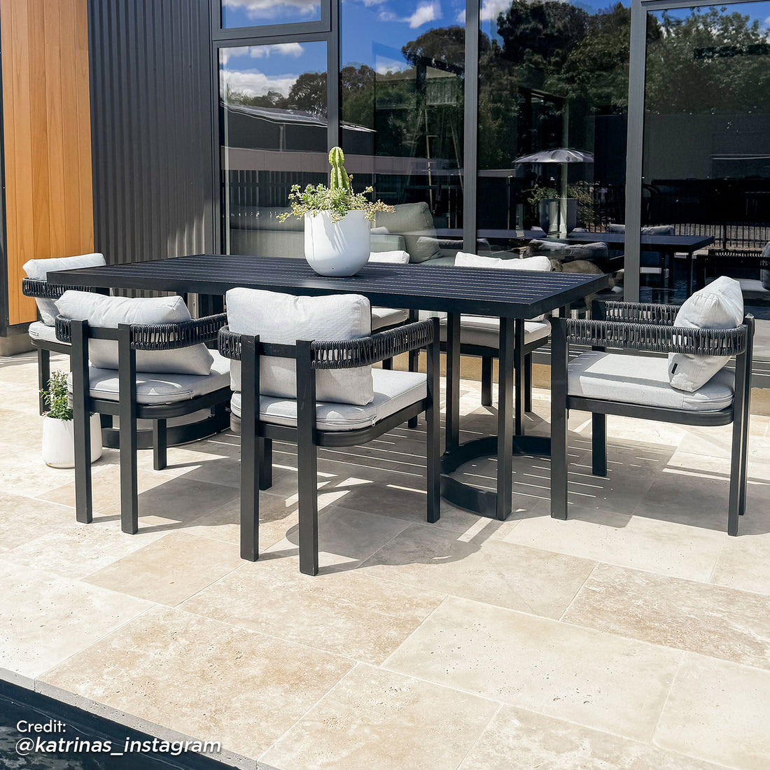 Tavari 208cm 6-Seater Curved Outdoor Dining Set in Black features a sleek black table and six chairs with woven rope-style armrests and light-gray cushions, set on a tiled patio.
