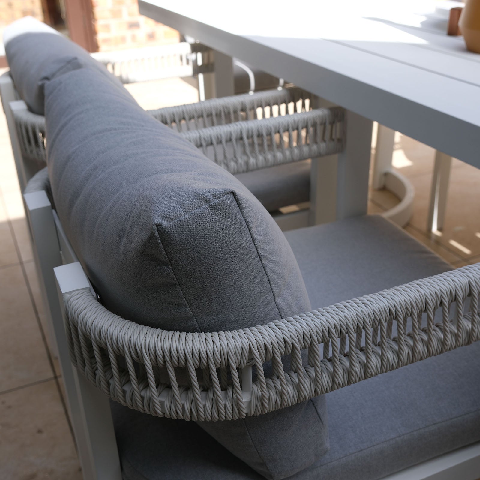 Tavari 6-Seater Aluminium Outdoor Dining Set in Light Grey featuring a modern bench with thick grey cushions and rope-wrapped armrests, accompanied by a matching chair and white rectangular table.