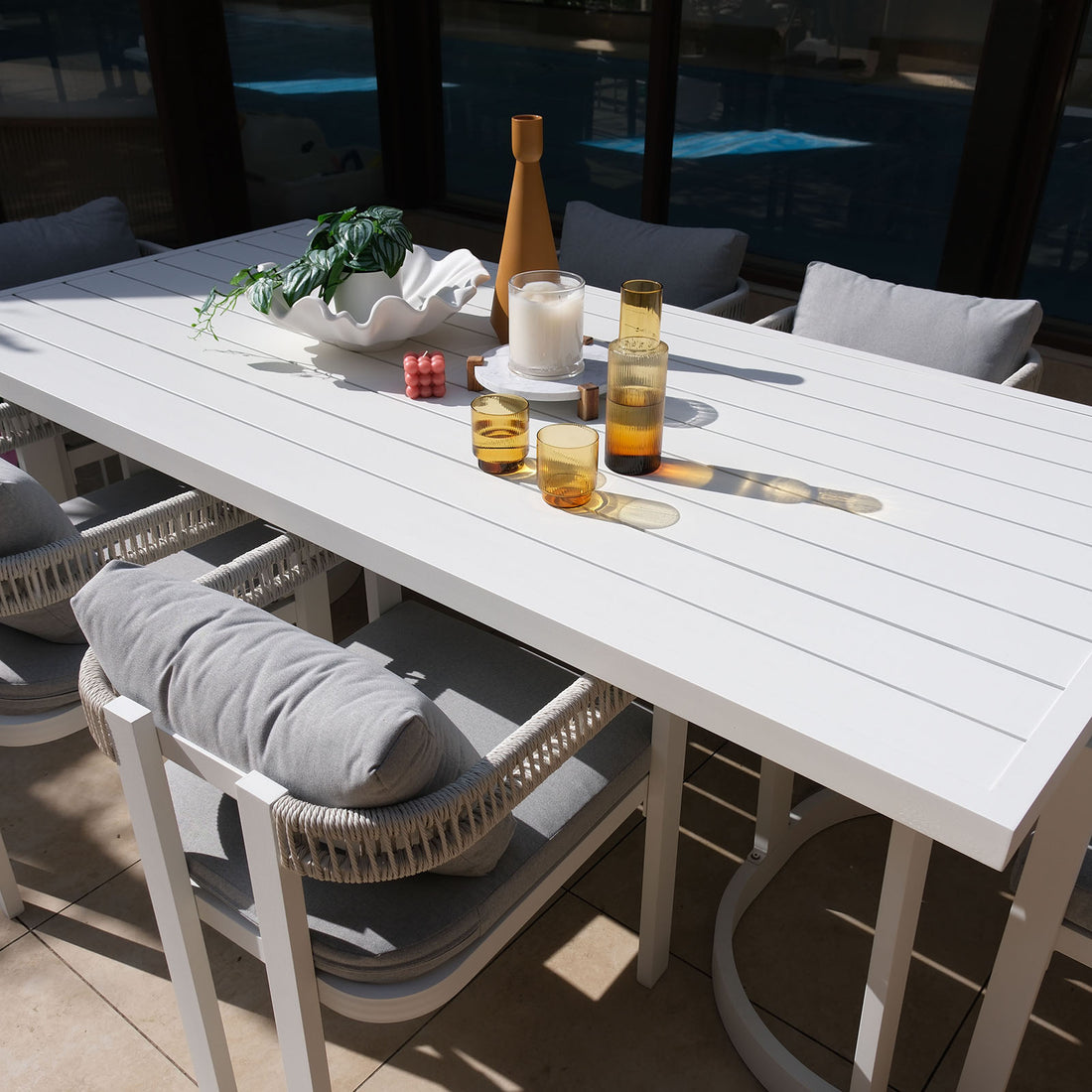 Tavari 6-Seater Aluminium Outdoor Dining Set in Light Grey features a sleek white slatted table, four cushioned chairs with woven armrests, and decorative tabletop items, perfect for stylish outdoor gatherings.