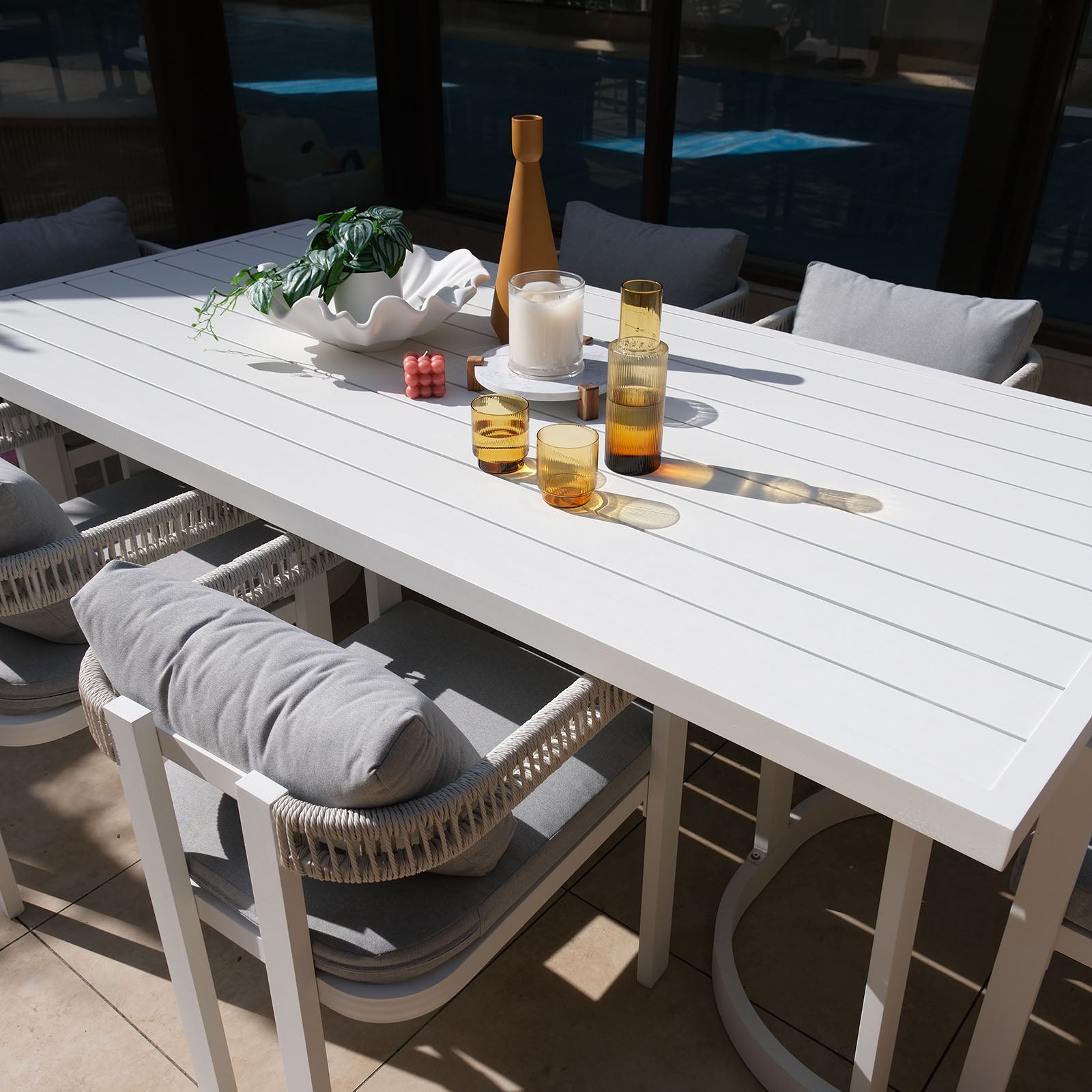 Tavari 6-Seater Aluminium Outdoor Dining Set in Light Grey features a sleek white slatted table, four cushioned chairs with woven armrests, and decorative tabletop items, perfect for stylish outdoor gatherings.