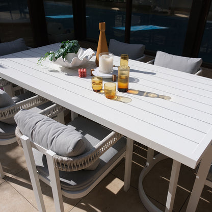 Tavari 6-Seater Aluminium Outdoor Dining Set in Light Grey features a sleek white slatted table, four cushioned chairs with woven armrests, and decorative tabletop items, perfect for stylish outdoor gatherings.