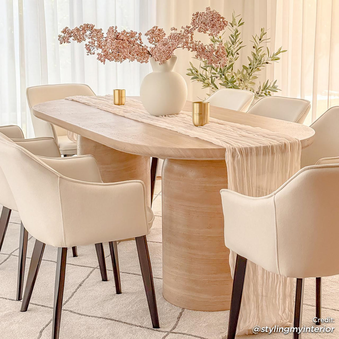 Tierre 200cm Concrete Indoor/Outdoor Dining Table in Beige, elegantly set with a blush runner and white vase, surrounded by cream armchairs, showcasing a modern, versatile aesthetic in a softly lit dining area.