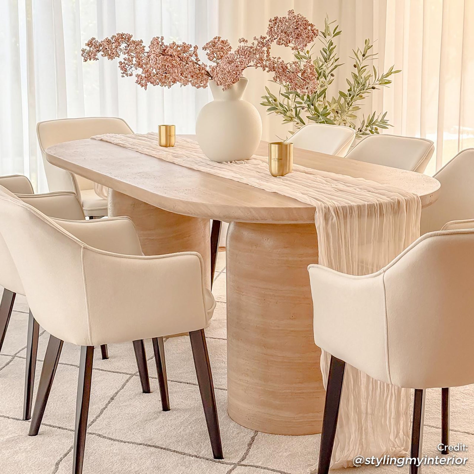 Tierre 200cm Concrete Indoor/Outdoor Dining Table in Beige, elegantly set with a blush runner and white vase, surrounded by cream armchairs, showcasing a modern, versatile aesthetic in a softly lit dining area.