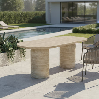 Tierre 200cm Concrete Outdoor Dining Table in Beige with an oval top and chunky cylindrical stone bases, set in a modern patio scene beside a pool with minimalist lounge chairs.