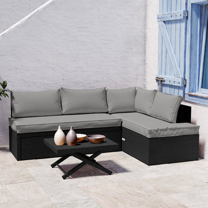 Tybee 4 Seater Rattan Outdoor Corner Sofa Set in Warm Grey features a black synthetic rattan sectional with light gray cushions and a matching coffee table, enhanced by decorative ceramic vases against a white stucco backdrop.