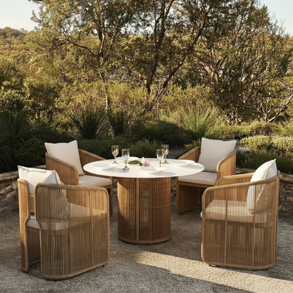 Vellora 4 Seater Wicker Outdoor Dining Set in Natural, featuring a round table with a woven base and four matching chairs, set amidst a garden backdrop, creating a serene outdoor dining scene.