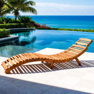 Wave Hardwood Acacia Foldable Outdoor Sun Lounger in Natural by an infinity pool, surrounded by tropical greenery and ocean view, showcasing its ergonomic wave design and sturdy, sustainable eucalyptus wood frame.