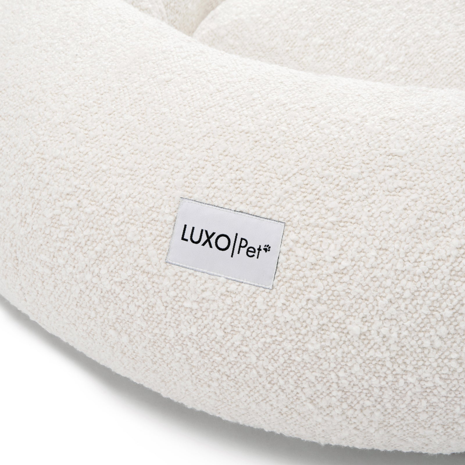 Kyra Large Boucle Pet Bed – Light Beige Plush Comfort featuring a close-up of white boucle fabric and a white label with black text, emphasizing its textured surface and premium design.
