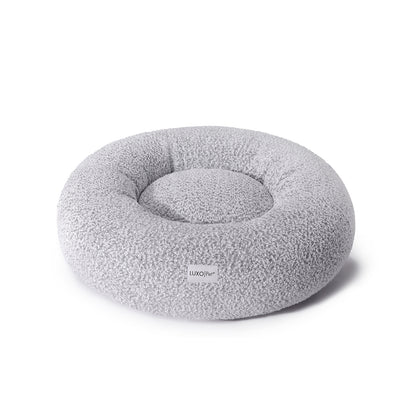 Kyra Medium Boucle Pet Bed – White with Black Base features a round, grey pillow design with soft curves and plush support, perfect for pets seeking comfort and modern style.