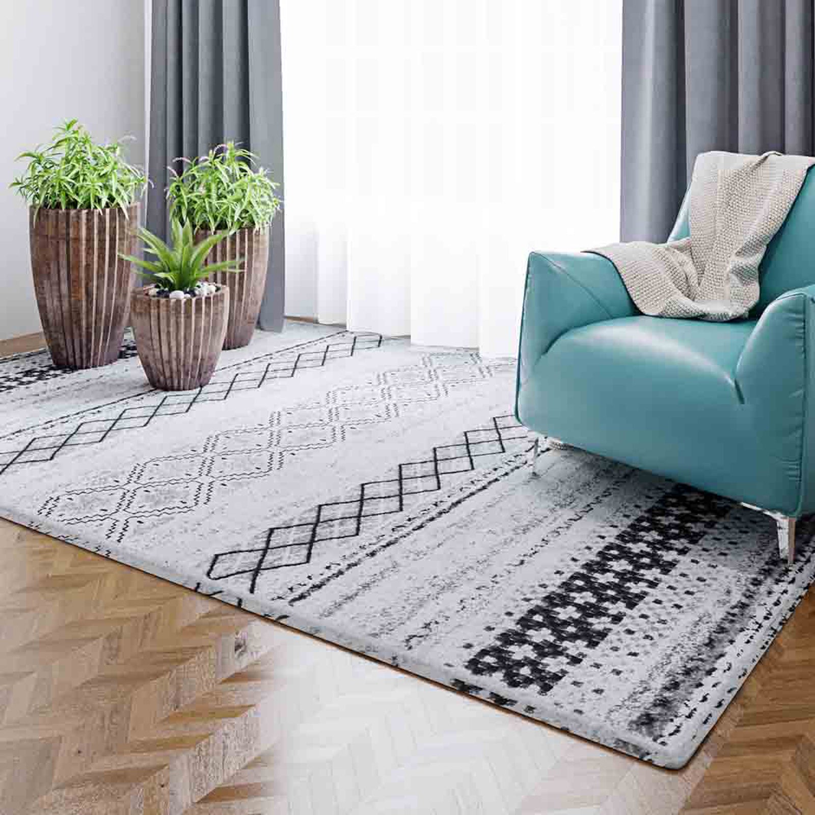 Alyne 200x300 Indoor Contemporary Large Floor Rug featuring light gray and off-white tones with black geometric patterns, complementing modern decor alongside teal-blue armchair and lush wooden planters.